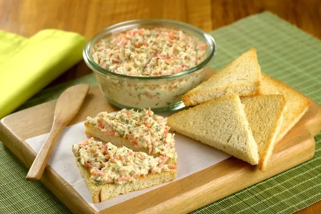 Tábua de madeira com uma tijela dee patê de frango com alho e torradas triangulares ao lado