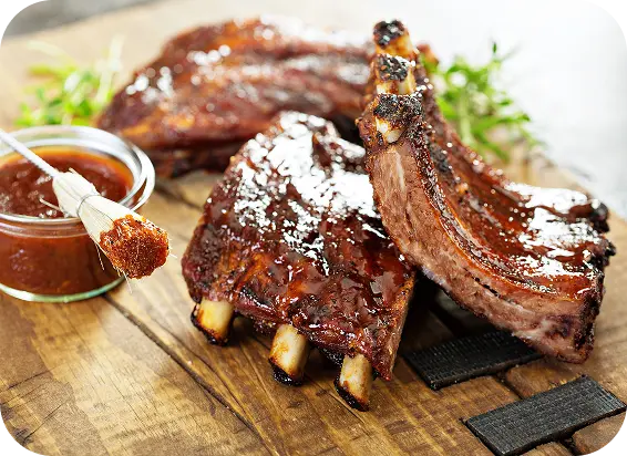 Tábua de madeira com pedaços de costela bovina e molho barbecue