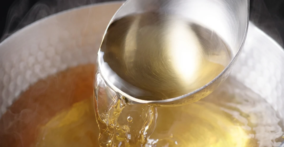 Colher despejando um líquido amarelado em uma panela